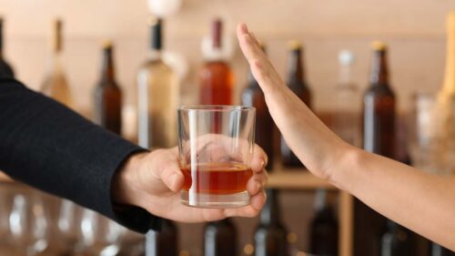 Man with glass of whiskey and woman refusing to drink in bar